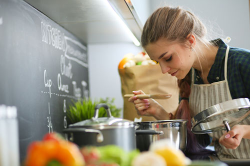 Young woman chef cooking at stove in the kitchen